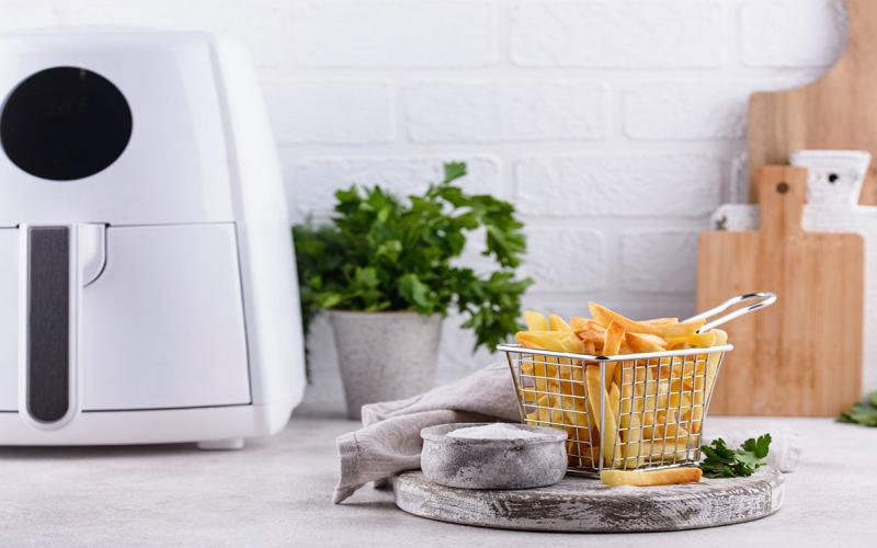 White basket-style air fryer on kitchen counter next to a basket of cooked French fries.