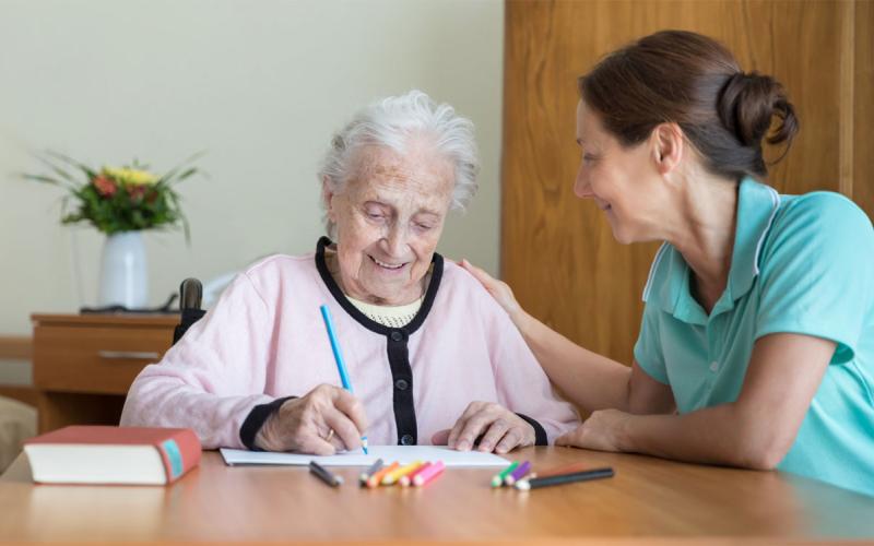 Caregiver assisting an older adult woman through a memory exercise.