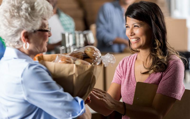 Woman delivering a bag food donations to a food bank manager.