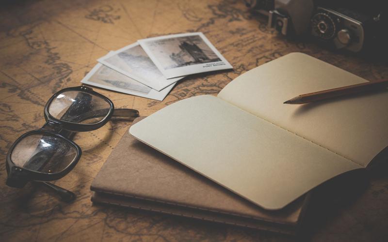 A blank notebook sitting by eye glasses and photos.