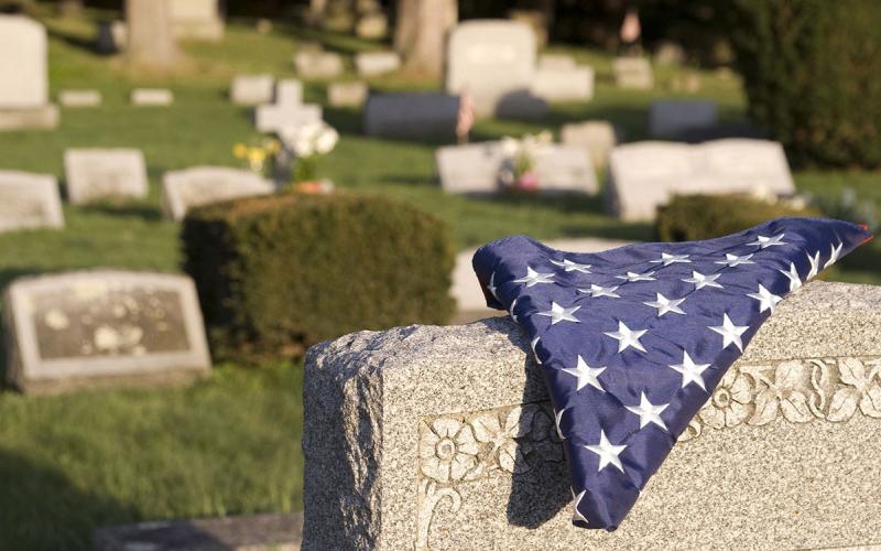A picture of a tombstone in a cemetery with an American flag laying on it.