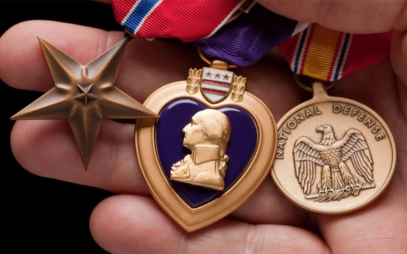 Hand holding Purple Heart, Bronze and National Defense War Medals.