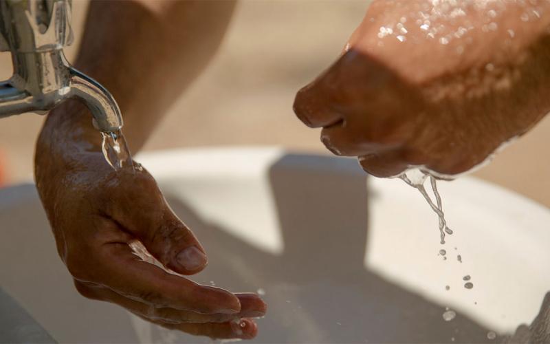 Man washing hands at an outdoor sink.