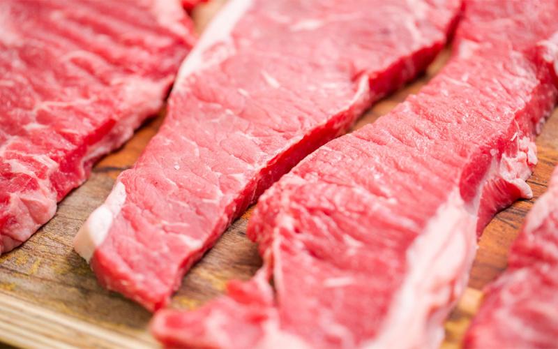 Raw New York strip steaks on a wood cutting board.
