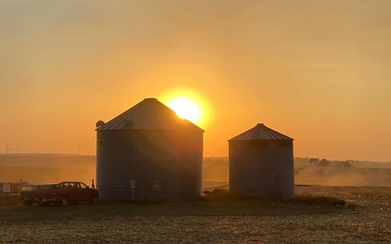 Sunset over two grain bins in a field.