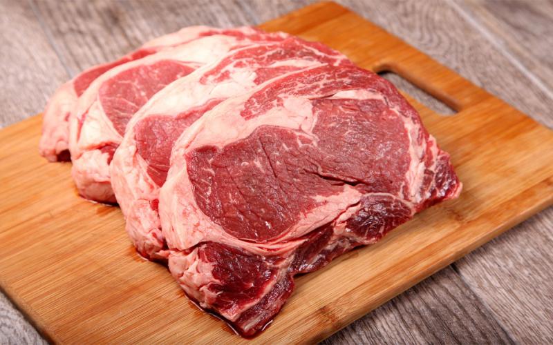 Three ribeye steaks on a cutting board.