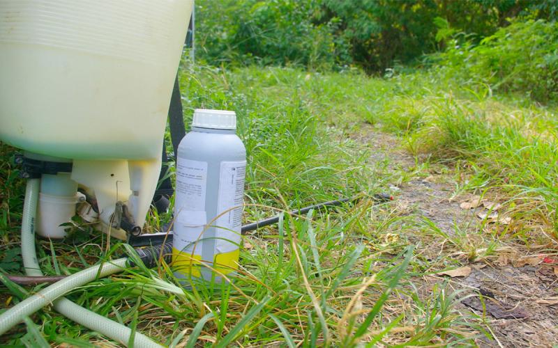Crop sprayer and a bottle of chemicals in a yard.