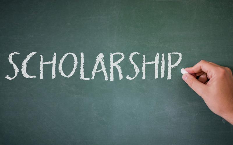 Hand writing the word “scholarship” on a chalk board.