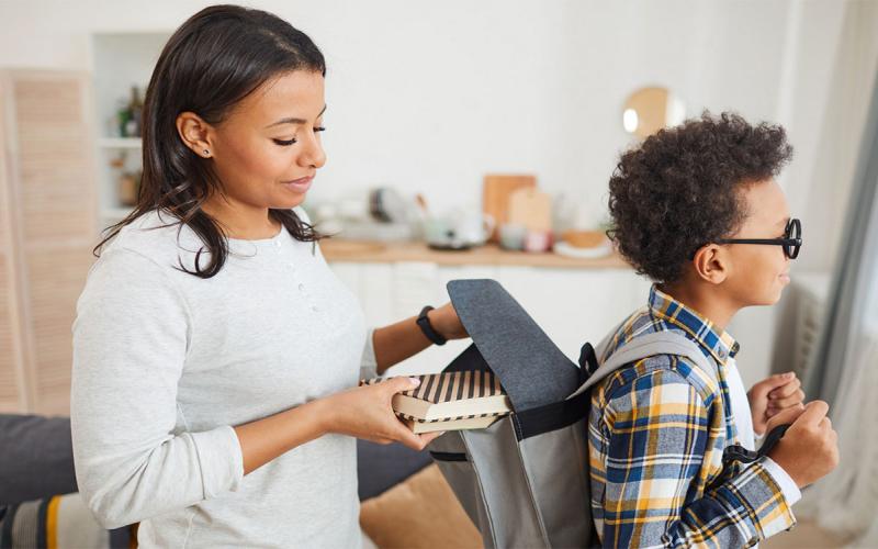 Mother helping her son prepare his school backpack.