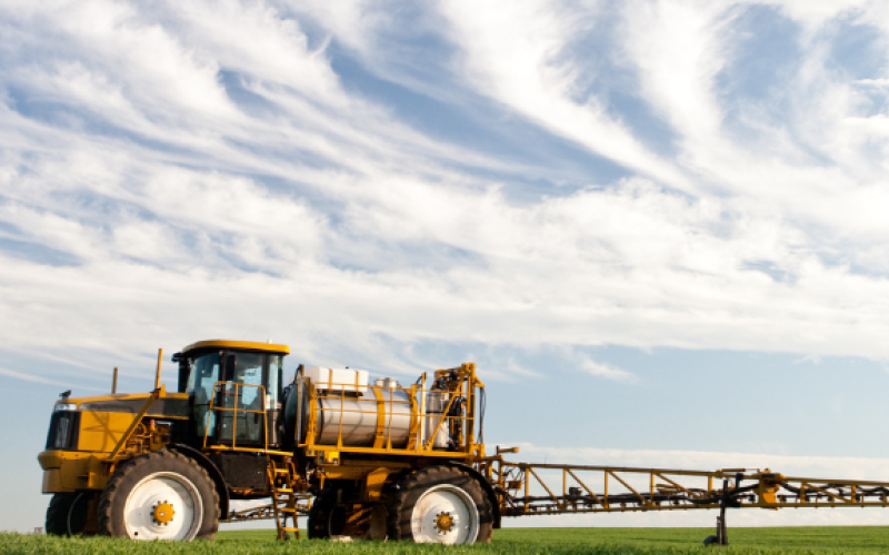 Sprayer in a field with a blue sky and wispy clouds on the horizon
