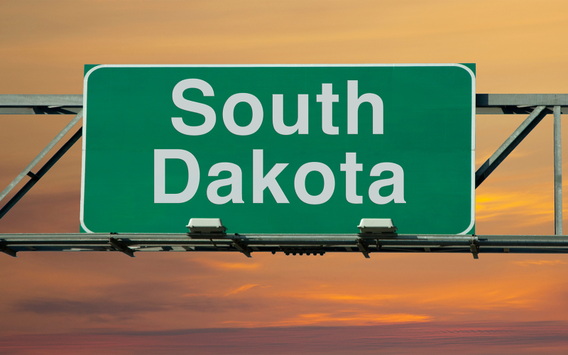 A green road sign that says South Dakota with the sunset in the background