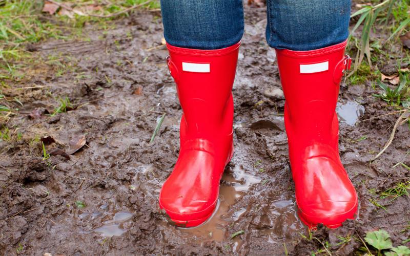 Gardener in red rain boots standing in a wet yard.