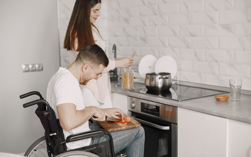 Man in a wheelchair cooking in an accessible kitchen with a woman.