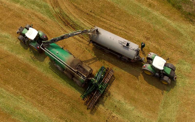 Tractor loading a liquid manure applicator in a bare field.