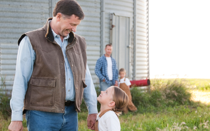 Older adult looking holding hands with young girl, while a father and son look on from a distance