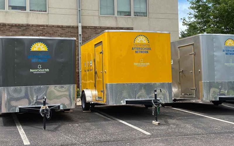 Three Think, Make, Create mobile lab trailers are parked in a lot with a building behind them.