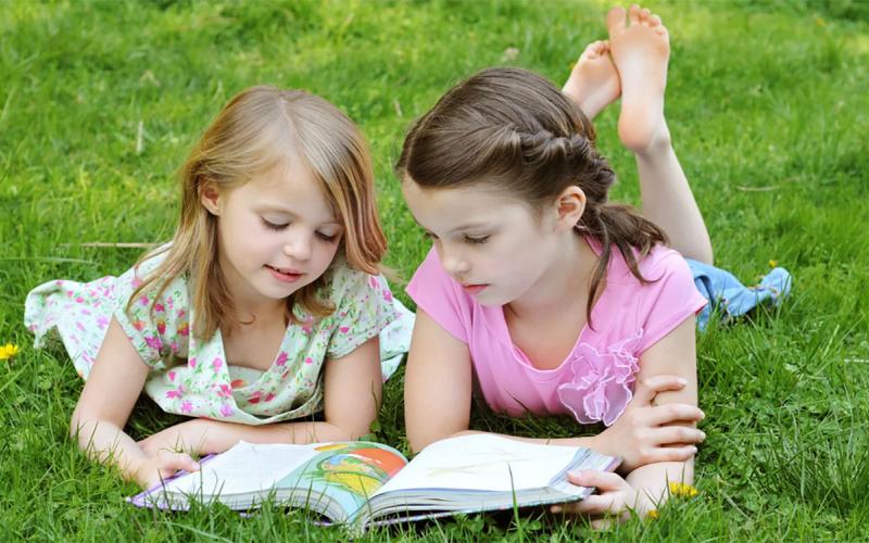 Two children reading a book on their lawn.