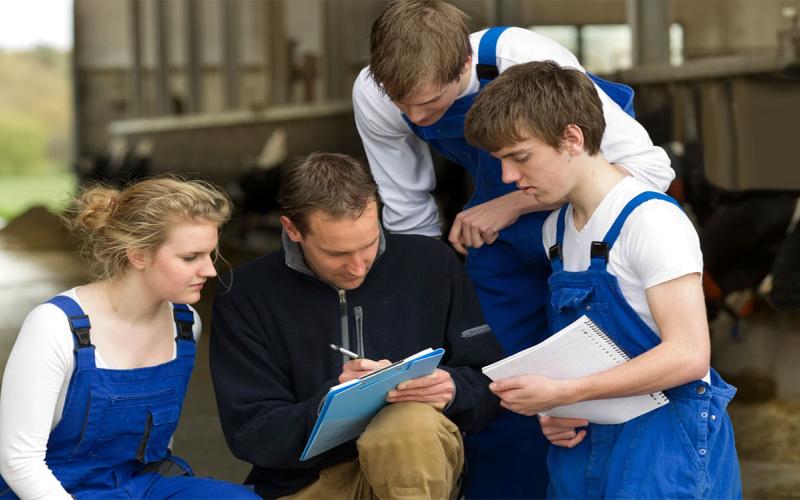 Group of farm trainees gathered around a veterinarian.