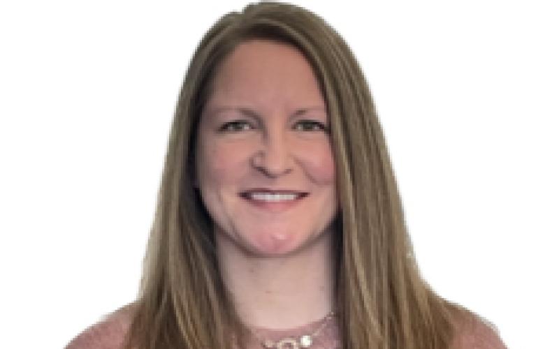 A woman stands against a white background smiling