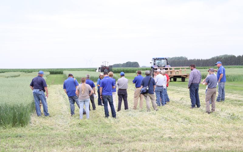 A group of people stand in a field with a combine in the background