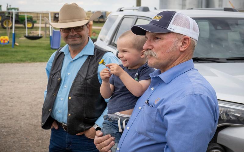 Father, son, and grandchild gathered at family farmyard.