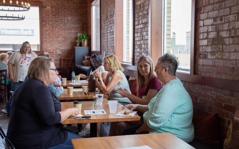 Three women sit at a booth in a small cafe.