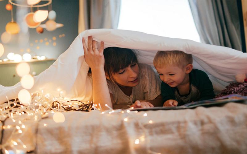 Mother and son reading bedtime story under a blanket.