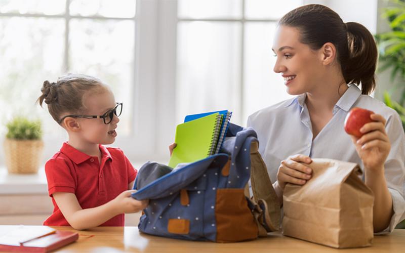 Mother and daughter packing backpack and brown lunch bag.