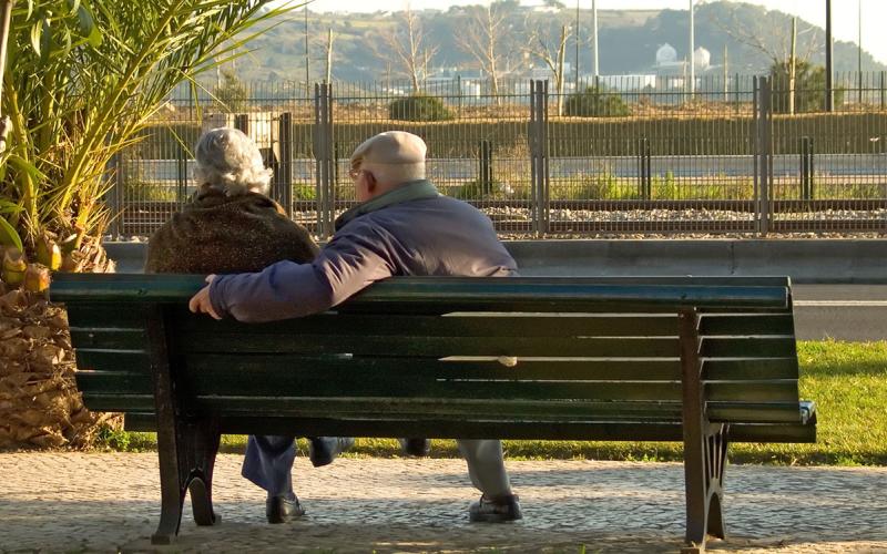 Retired couple sitting on a park bench overlooking a bluff.