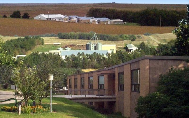 The University of Nebraska Lincoln Haskell Lab is pictured, a brown brick building in the foreground with fields and farm buildings in the background