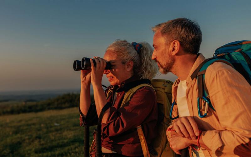 Middle-age couple uses binoculars during a sunset hike.