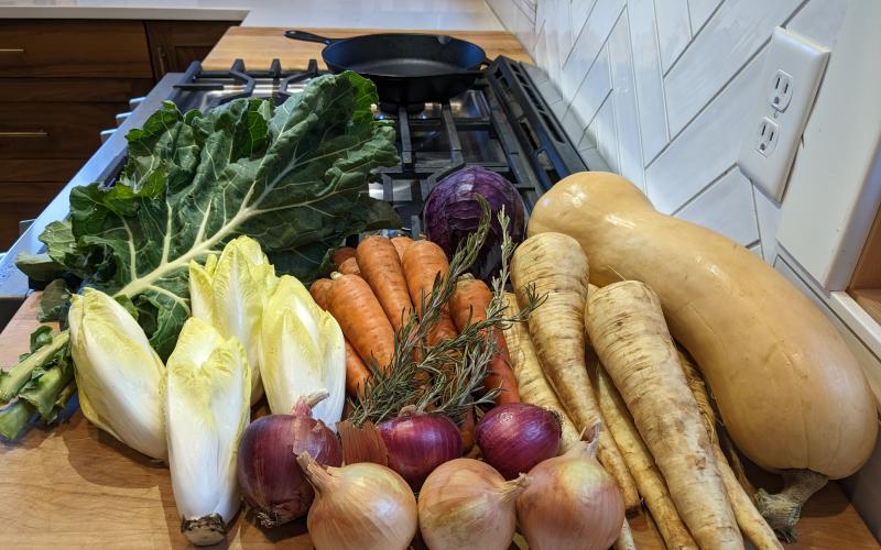 fresh vegetables including onions, potatoes, lettuce and squash are shown piled on a counter