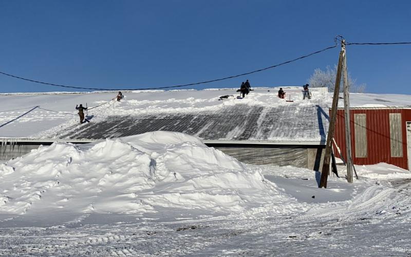 Small crew of workers removing snow from the roof of a pole barn.
