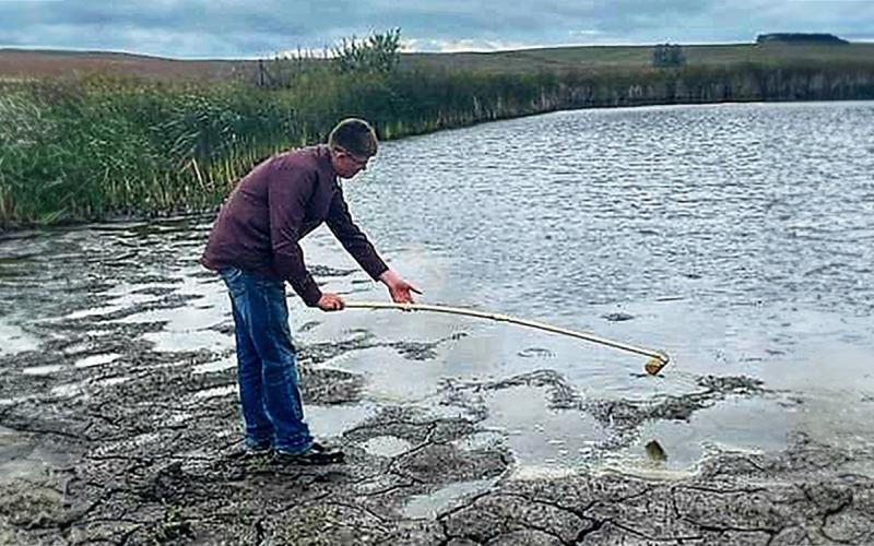 A young man collecting a water sample from a pond using a water dipper.