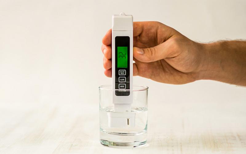 Hand holding a TDS meter in a water container.