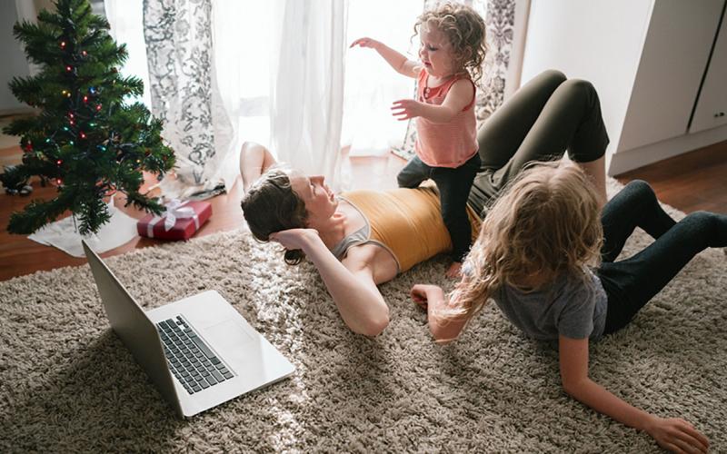 Mother and two daughters doing an online family fitness routine near a small Christmas tree.