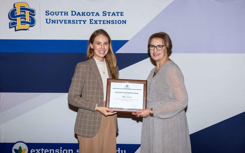 Megan Jacobson smiles at the camera with the certificate she's receiving from Karla Trautman