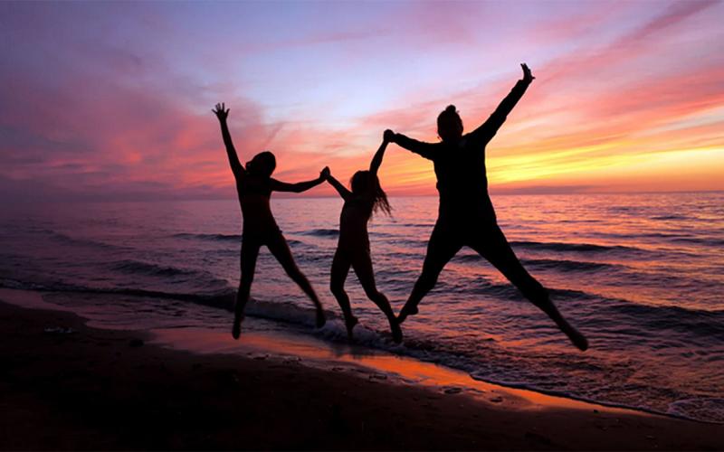Silhouettes of three women jumping on the beach at sunset.