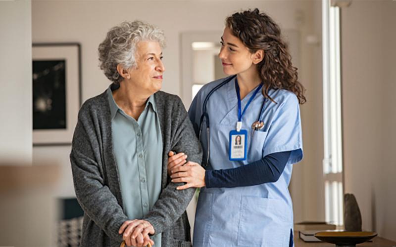 Young nurse escorting an older adult at a hospital.
