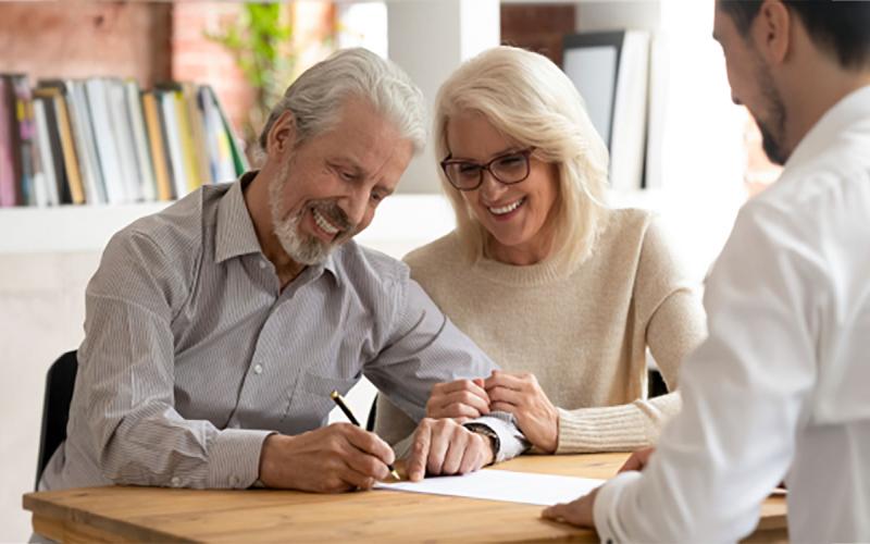 An older couple reviewing and signing paperwork with a health care professional.