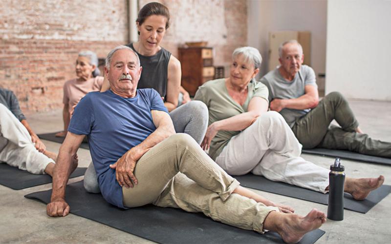 Yoga instructor helping a group of older adults with stretching exercises.