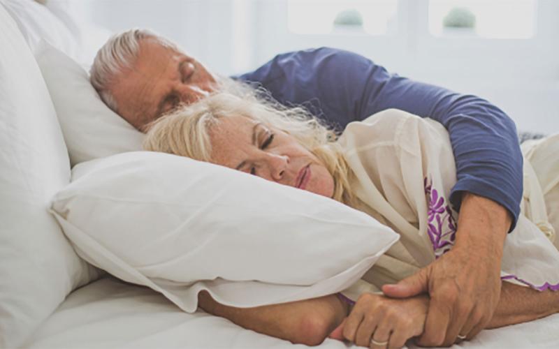 An older couple asleep in their bed.
