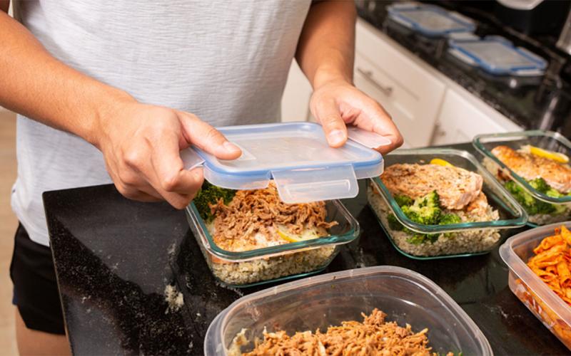 Man preparing several batches of pre-cooked meals for the week in plastic containers.