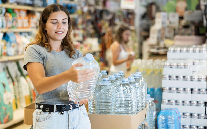 Young woman reading the nutrition facts label on a large bottle of water at the grocery store.