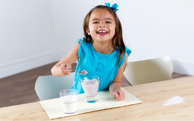 Young girl eating yogurt at a kitchen table.