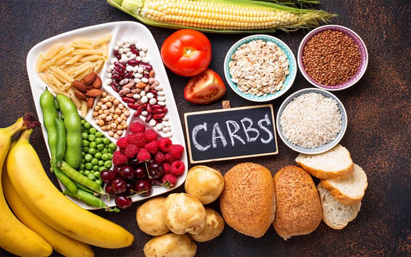 Chalkboard with the word “Carbs” written on it among several healthy food sources of carbohydrates.