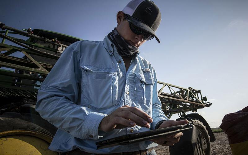Young farmer analyzing data on a tablet computer beside a crop sprayer.