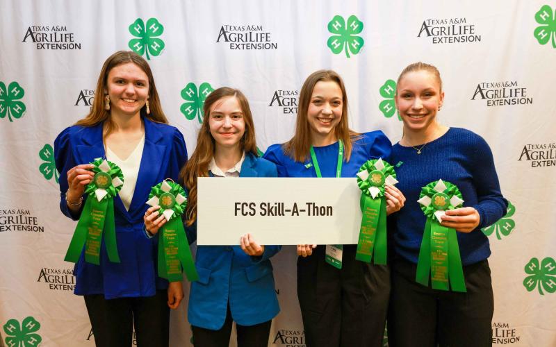 The four members of the South Dakota FCS Skill-a-Thon stand with their green ribbons and holding a white sign that says FCS Skill-a-Thon at the 2024 National 4-H FCS Championship and Conference