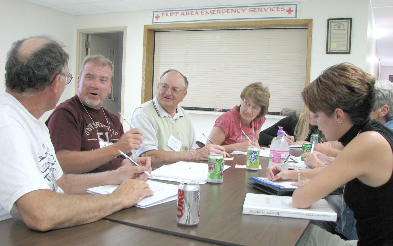 About six people sit around a table in a community room with notebooks and pens