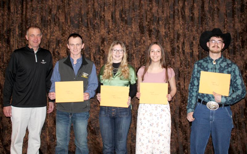 four students smile at the camera holding large manila envelopes next to the man who presented them with the scholarships